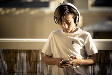 Boy listening music with headphones and smartphone on balcony - SIPF000123