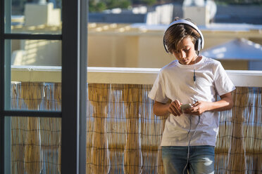 Junge hört Musik mit Kopfhörern und Smartphone auf dem Balkon - SIPF000124