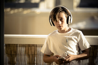 Portrait of boy listening music with headphones and smartphone on balcony - SIPF000125