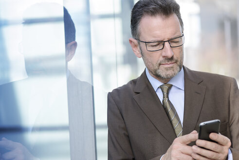 Portrait of businessman with spectacles using smartphone - GUFF000246