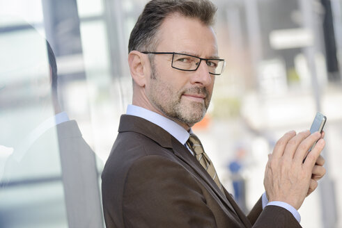Portrait of businessman with spectacles and smartphone - GUFF000251
