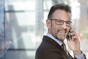 Portrait of smiling businessman telephoning with smartphone - GUFF000252