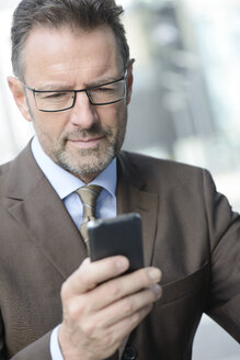 Porträt eines Geschäftsmannes mit Brille, der auf sein Smartphone schaut - GUFF000254