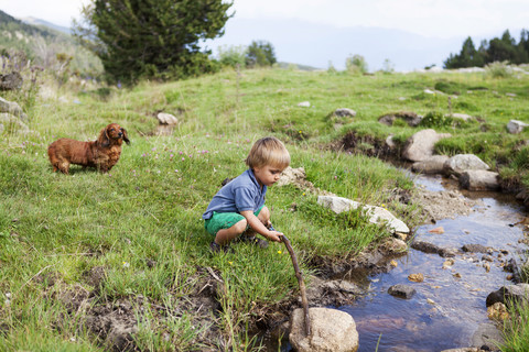 Spanien, Cerdanya, kleiner Junge spielt auf einer Wiese an einem Bach, lizenzfreies Stockfoto