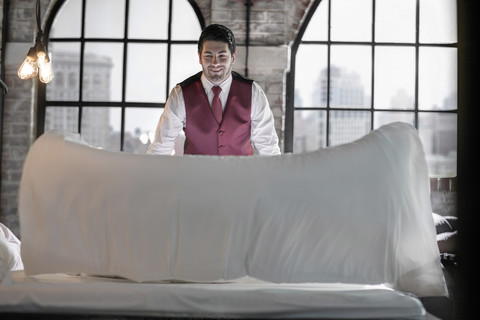 Butler im Hotelzimmer, macht das Bett, lizenzfreies Stockfoto