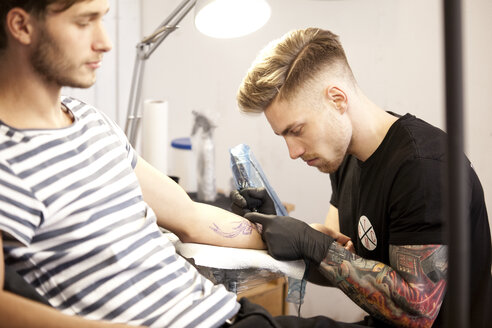 Tätowierer bei der Arbeit in seinem Tattoo-Studio - MFRF000488