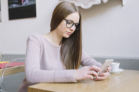 Junge Frau sitzt in einem Café und schaut auf ihr Smartphone, lizenzfreies Stockfoto