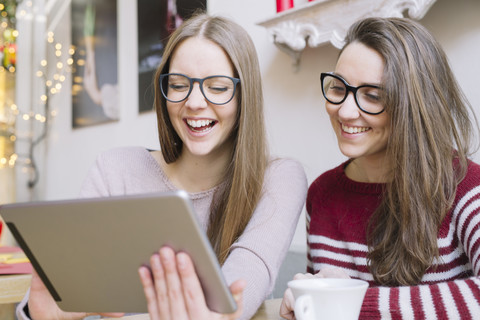 Zwei junge Frauen amüsieren sich in einem Café mit einem digitalen Tablet, lizenzfreies Stockfoto