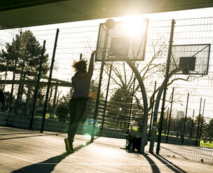 Rückenansicht einer jungen Frau, die auf einem Spielfeld einen Basketball wirft - MADF000775