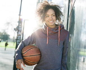 Portrait of smiling young woman with basketball at backlight - MADF000778