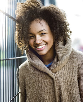 Porträt einer lächelnden jungen Frau, die sich an einen Zaun lehnt - MADF000781