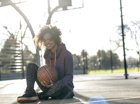 Porträt einer lächelnden jungen Frau mit Basketball auf einem Spielfeld, lizenzfreies Stockfoto