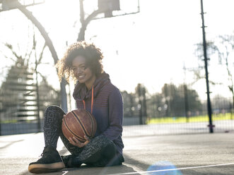 Porträt einer lächelnden jungen Frau mit Basketball auf einem Spielfeld - MADF000786