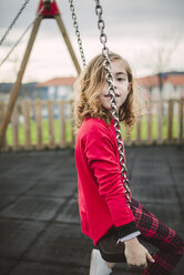 Little blonde girl wearing red pullover sitting on a swing - RAEF000815