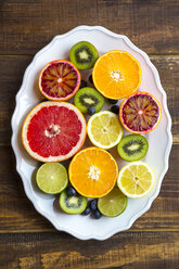 Plate of blueberries, kiwis and sliced citrus fruits on wood - SARF002494