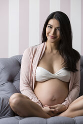 Lächelnde schwangere Frau in Unterwäsche auf einem Sessel sitzend - SHKF000477