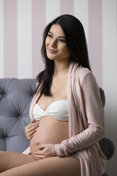 Smiling pregnant woman in lingerie sitting on armchair - SHKF000478