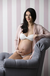 Happy pregnant woman kneeling on the floor in a studio, smiling at