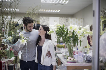 Happy young couple with bunch of flowers leaving flower shop - ZEF008128