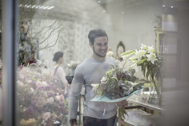 Lächelnder junger Mann mit Blumenstrauß beim Verlassen eines Blumenladens - ZEF008129