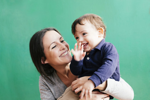 Porträt einer glücklichen Mutter mit ihrem kleinen Sohn vor einem grünen Hintergrund, lizenzfreies Stockfoto