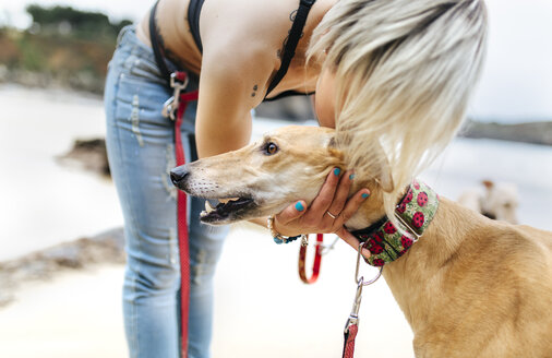 Spanien, Llanes, junge Frau mit ihrem Windhund am Strand - MGOF001299