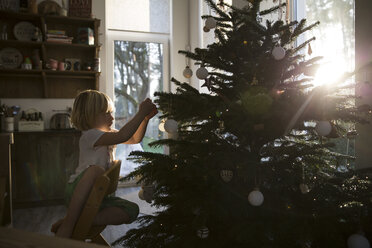 Mädchen beim Schmücken des Weihnachtsbaums im Gegenlicht - FKF001672