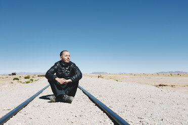 Bolivien, Zugfriedhof Uyuni, Mann sitzt auf der Eisenbahn und schaut in die Ferne - GEMF000667