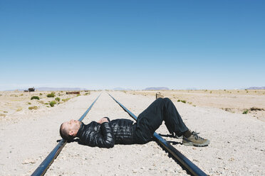 Bolivia, Uyuni train cemetery, man lying on train tracks - GEMF000668