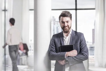 Porträt eines lächelnden Geschäftsmannes, der ein digitales Tablet im Büro hält - ZEF008135