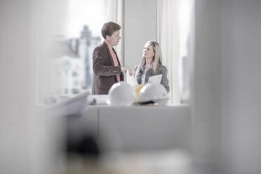 Man talking to woman in office with hard hats on table - ZEF008150