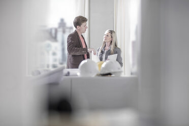 Mann spricht mit Frau in Büro mit Schutzhelmen auf Tisch - ZEF008150