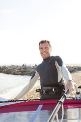 Lächelnder Mann am Strand mit Surfbrett - VABF000096