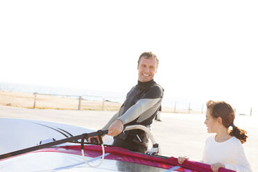 Lächelnder Mann mit Tochter an der Küste mit Surfbrett - VABF000107