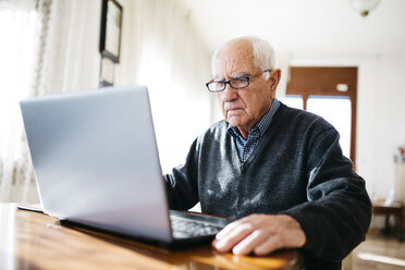 Porträt eines ernst dreinblickenden älteren Mannes, der zu Hause einen Laptop benutzt - JRFF000356