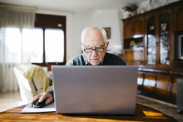 Porträt eines ernst dreinblickenden älteren Mannes, der zu Hause einen Laptop benutzt - JRFF000357