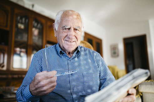 Porträt eines lächelnden älteren Mannes mit Zeitung zu Hause - JRFF000375
