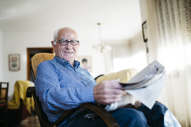 Portrait of smiling senior man with newspaper at home - JRFF000377