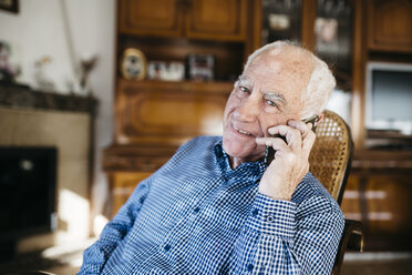 Porträt eines lächelnden älteren Mannes, der zu Hause mit seinem Smartphone telefoniert - JRFF000383