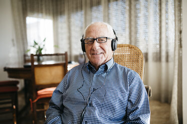 Portrait of smiling senior man hearing music with headphones at home - JRFF000384