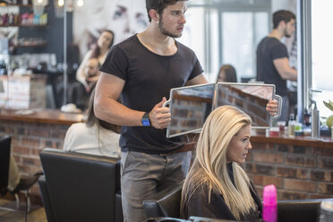 Woman in hair salon checking hair in mirror - ZEF008218