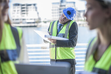 Ingenieur auf einer Baustelle, der einen Bauplan hält und telefoniert - ZEF008241