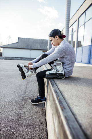 Junger Mann sitzt auf einer Rampe und zieht Inline-Skates an, lizenzfreies Stockfoto