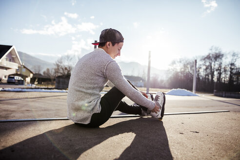Junger Mann sitzt auf einer Rampe und zieht Inline-Skates an - DAWF000491