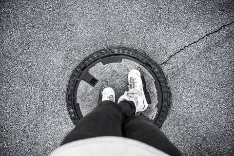 Junger Mann mit Inline-Skates auf einem Kanaldeckel stehend, lizenzfreies Stockfoto