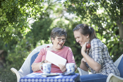 Großmutter und Enkelin im Garten, die gemeinsam auf ein digitales Tablet schauen, lizenzfreies Stockfoto