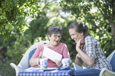 Grandmother and granddaughter in garden together looking at digital tablet - ZEF008279