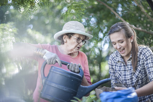 Senior woman and teenage girl watering plant in garden - ZEF008285