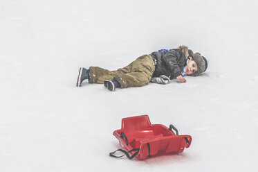 Boy lying in snow next to sledge - DEGF000606
