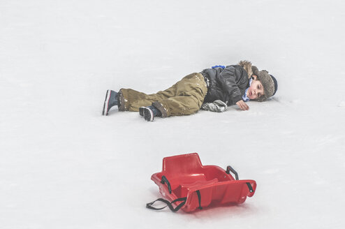 Junge im Schnee liegend neben Schlitten - DEGF000606